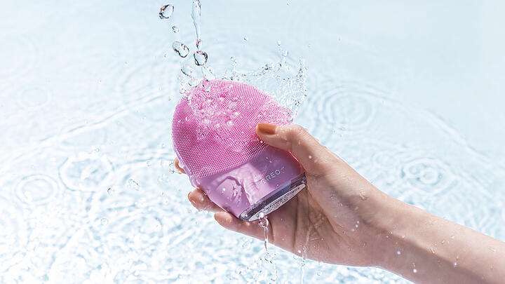 Hand holding FOREO LUNA 4 facial cleansing device under water